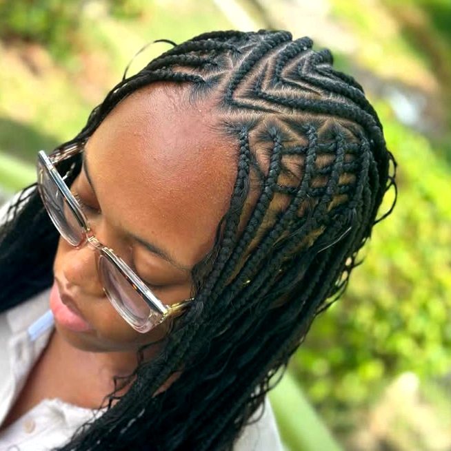 A close-up of a woman with flip-over Fulani braids hairstyle featuring intricate cornrow patterns on top and long, braided hair flowing down.