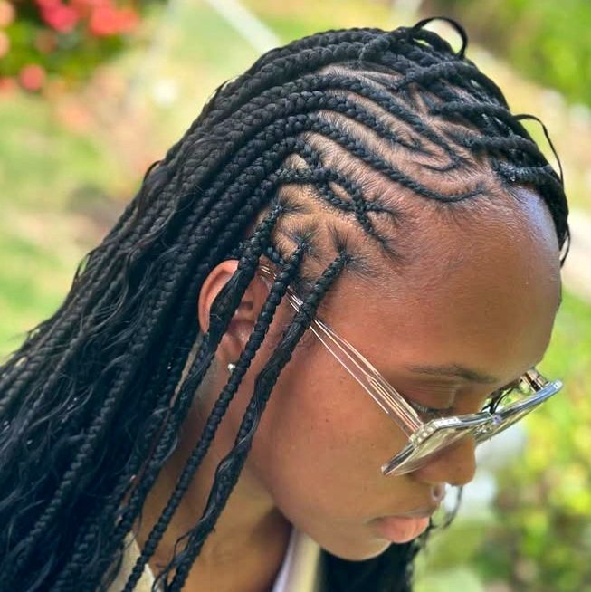 A close-up view of a woman's head showcasing flip-over Fulani braids. The hairstyle features knotless braids with cornrows on the sides, emphasizing the intricate patterns and textures of the braids.