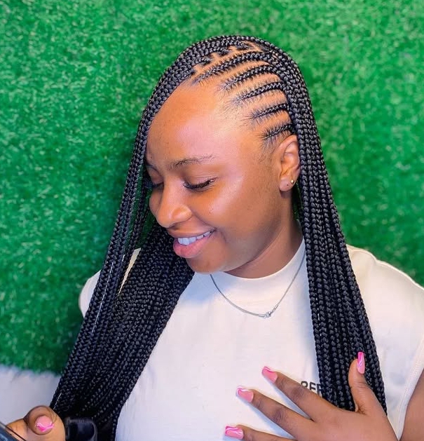 A close-up of a woman smiling while showcasing her flip-over Fulani braids hairstyle, with intricate cornrows on one side and long knotless braids flowing freely.