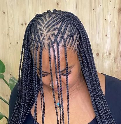 Close-up of a woman's head showcasing flip-over Fulani braids hairstyle, featuring intricate cornrows and long box braids, set against a natural wooden background.