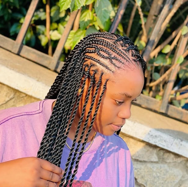 A side profile of a person with flip-over Fulani braids, featuring a blend of cornrows and knotless braids, set against a leafy outdoor backdrop.