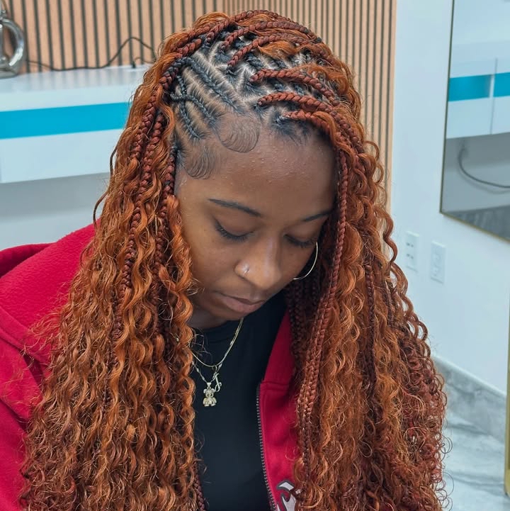 A woman with flip-over Fulani braids featuring a mix of knotless braids and cornrows, styled with curly ends in a vibrant orange color.
