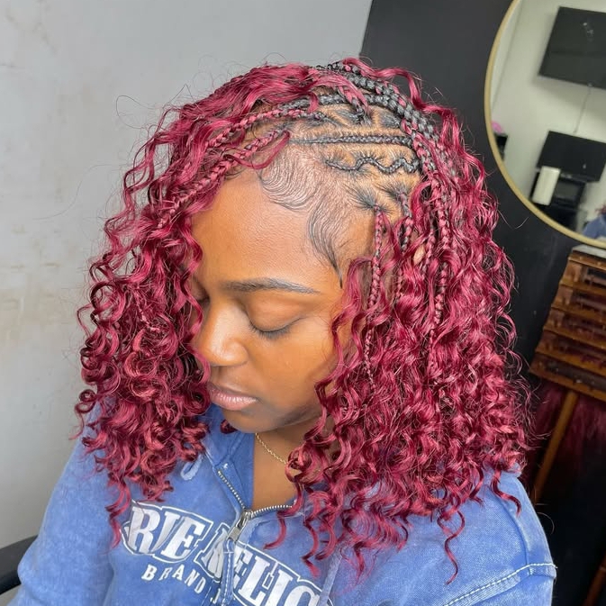 A woman showcasing a flip-over Fulani braids hairstyle with burgundy curly hair and cornrows on the sides, wearing a blue hoodie.