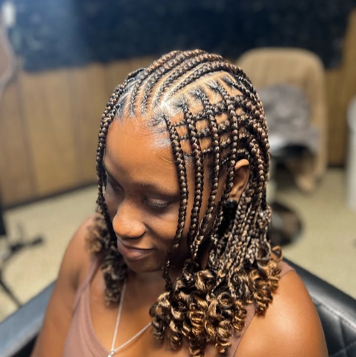 A woman with flip-over Fulani braids hairstyle, featuring knotless braids and curly ends, showcasing intricate cornrow patterns on the sides.