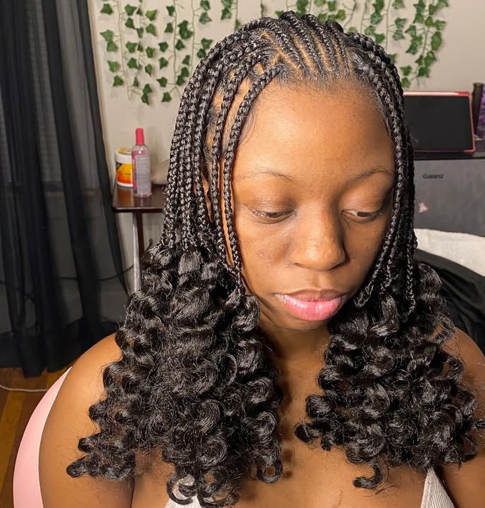 A close-up view of a person with flip-over Fulani braids featuring braided sections at the top and curly ends, showcasing a protective hairstyle that combines knotless braids and curls.