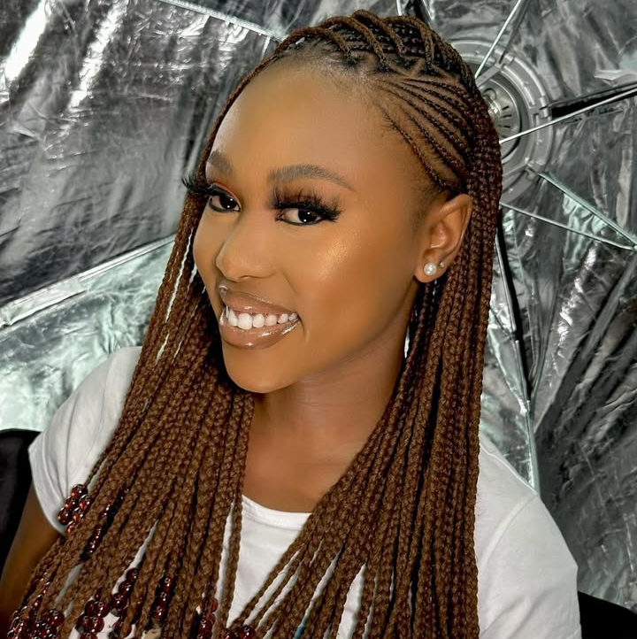 Young woman with flip-over Fulani braids hairstyle featuring brown braids and decorative beads, smiling in front of a reflective backdrop.