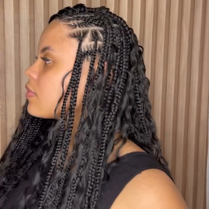A side profile of a woman with flip-over Fulani braids hairstyle, featuring knotless braids and cornrows, set against a light wooden backdrop.