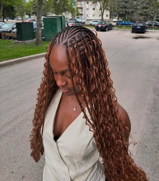 A woman with flip-over Fulani braids hairstyle featuring a blend of knotless box braids and curly ends. She is wearing a sleeveless outfit and standing in a park-like setting.