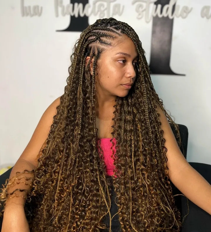 A woman with long, curly flip-over Fulani braids, showcasing a blend of knotless box braids and cornrows, sitting in a salon environment.