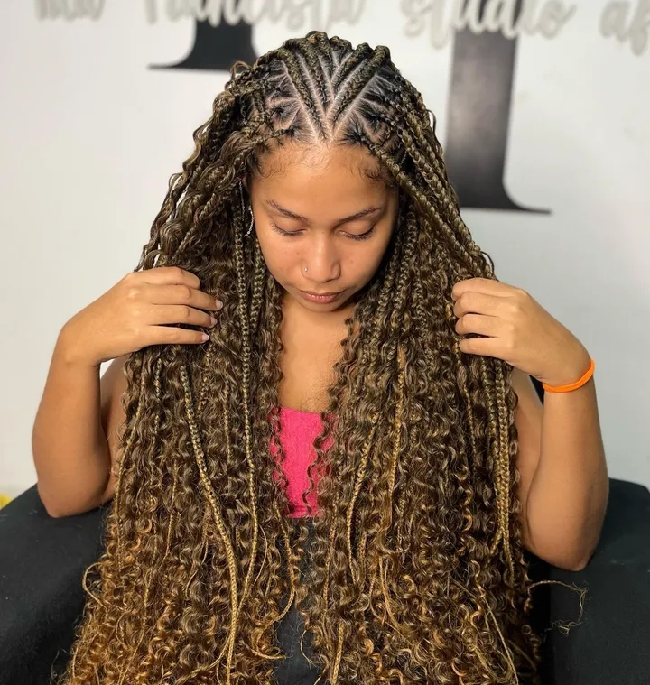 A woman with long, curly flip-over Fulani braids hairstyle, showcasing the intricate cornrow pattern at the top and the length of the curls cascading down her back.